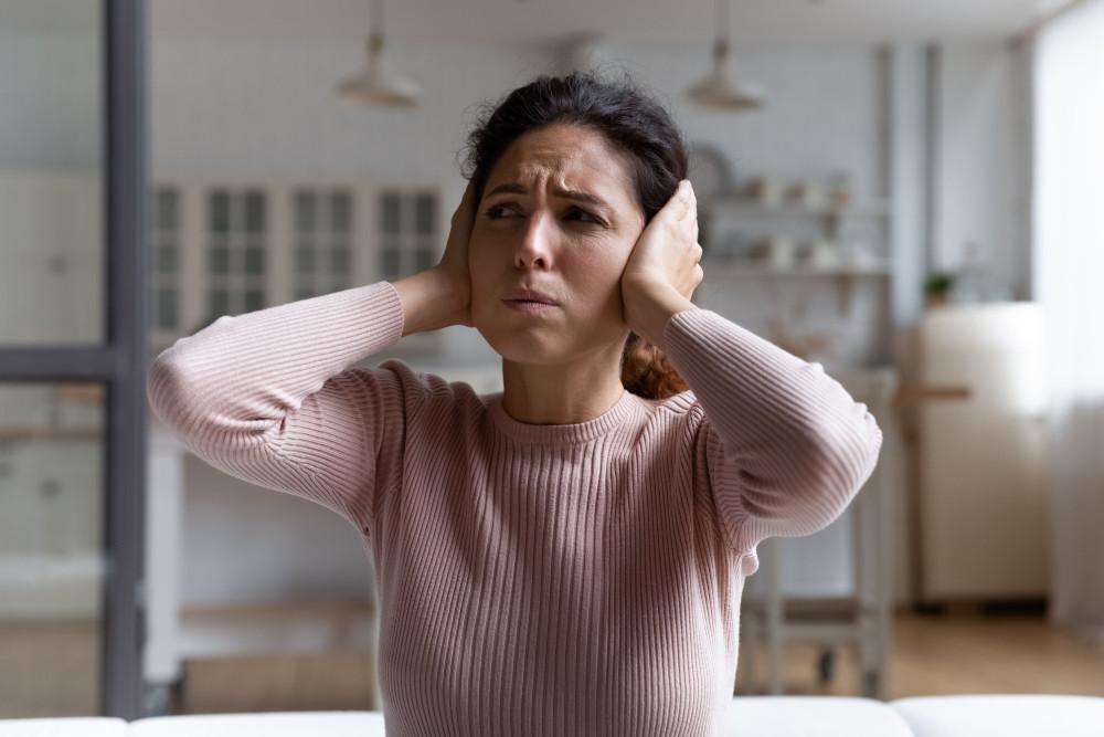 Mulher com as mãos sobre os ouvidos, expressão de desconforto com o zumbido
